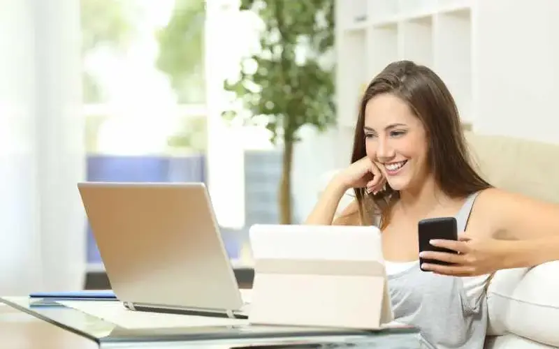 Imagem de uma mulher sorrindo em frente a um notebook e um tablet