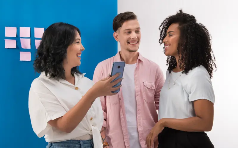 Imagem de 3 pessoas conversando e olhando para um celular.